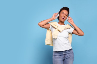 Photo of Happy young woman in headphones dancing on light blue background. Space for text