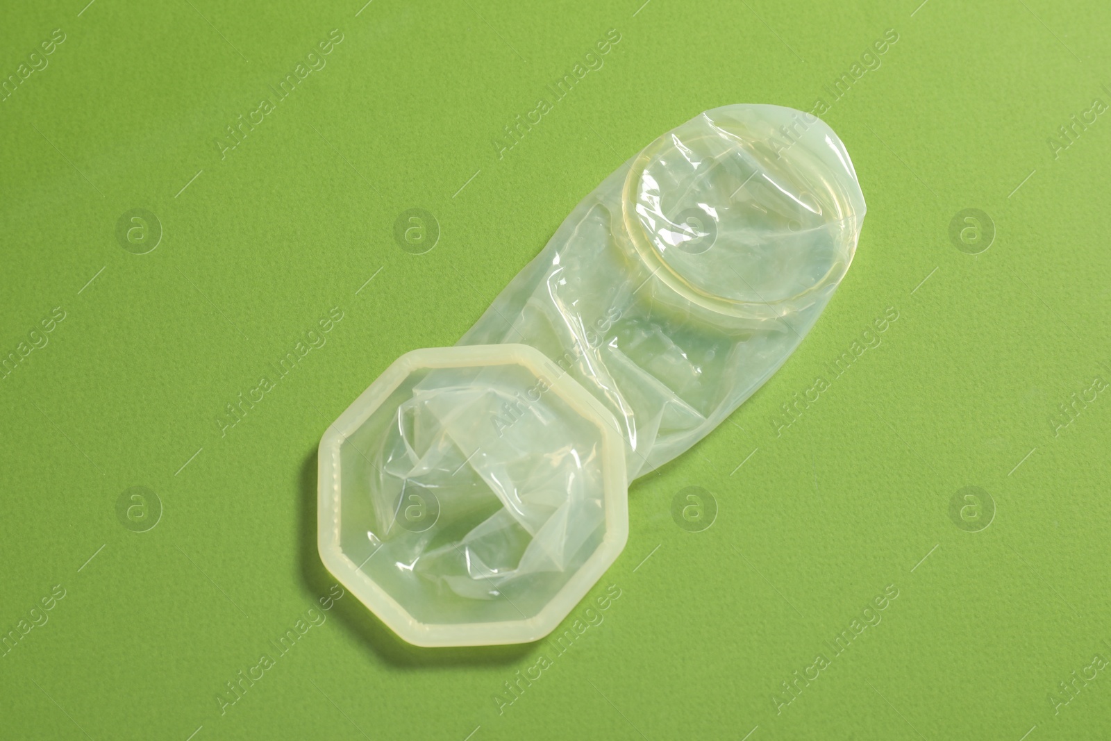 Photo of Unrolled female condom on green background, top view. Safe sex
