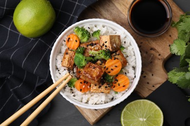 Delicious rice with fried tofu, broccoli and carrots served on grey wooden table, flat lay