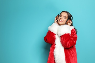 Photo of Young woman in Santa costume listening to Christmas music on color background