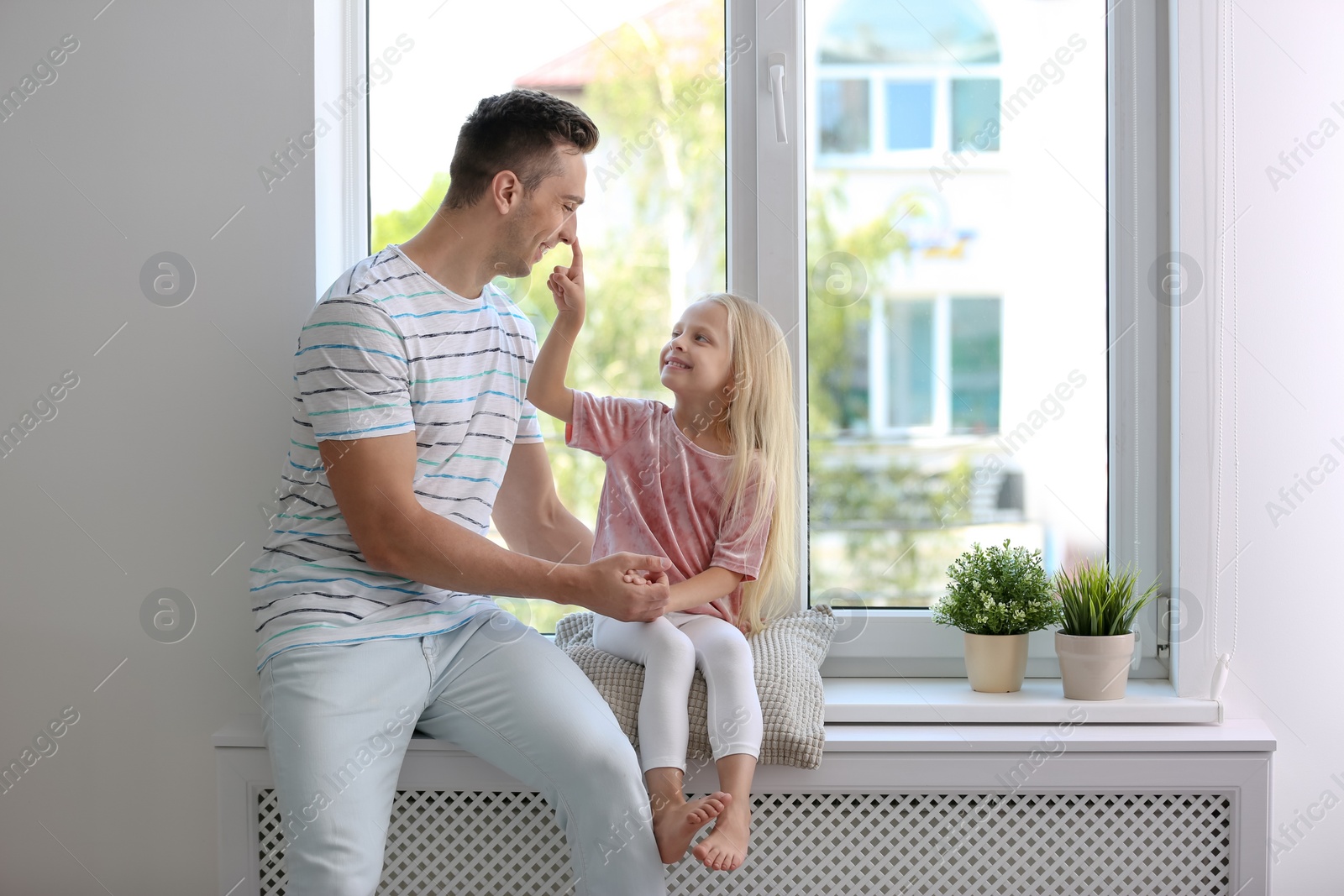 Photo of Young man with cute little girl near window at home