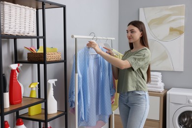 Photo of Beautiful young woman taking shirt from rack in laundry room