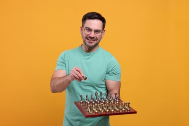 Photo of Smiling man holding chessboard with game pieces on orange background