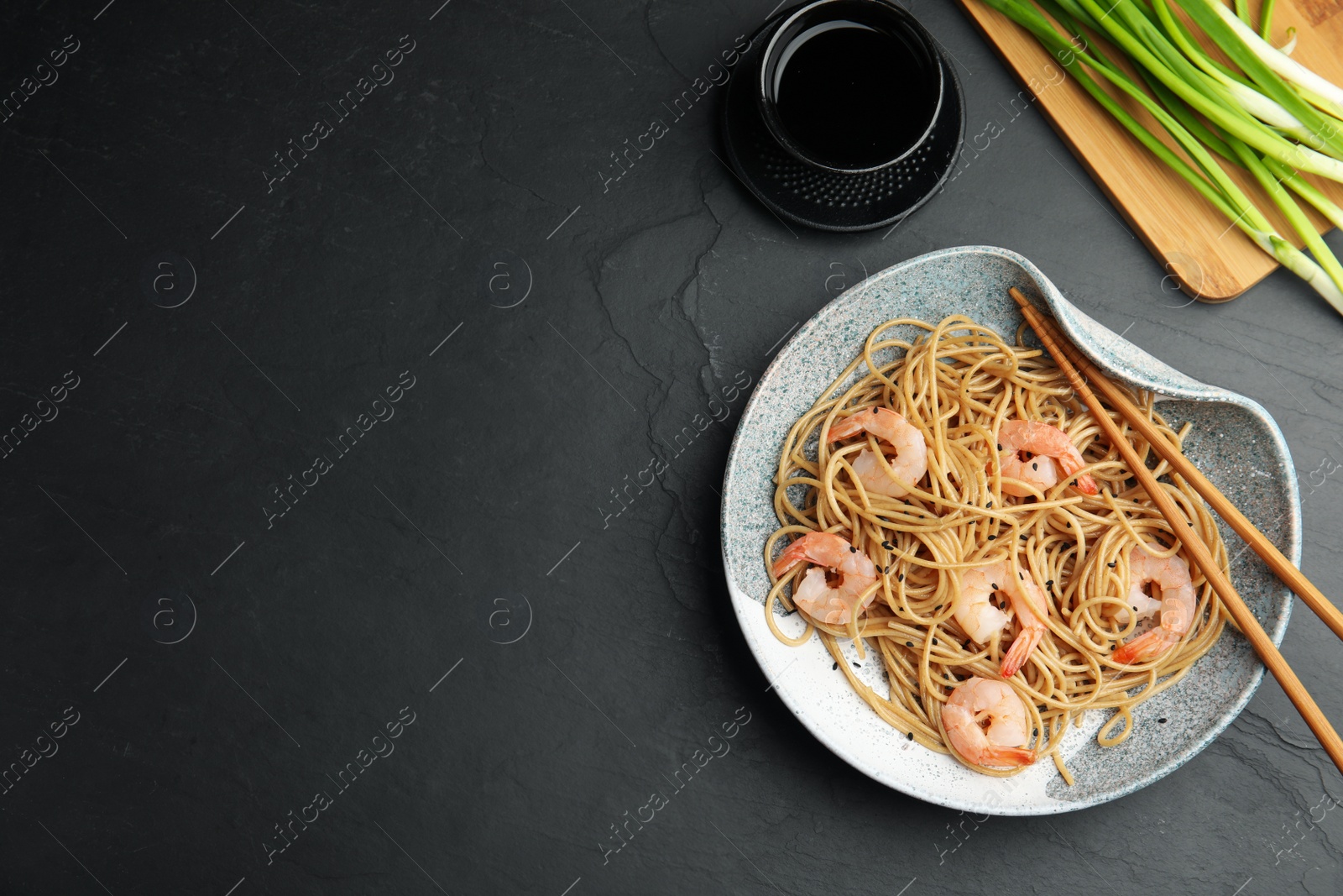 Photo of Tasty buckwheat noodles with shrimps served on black table, flat lay. Space for text