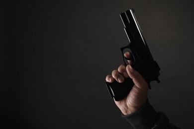 Photo of Armed robbery. Dangerous criminal with gun on black background, closeup. Space for text