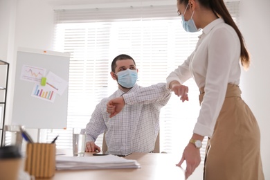 Photo of Coworkers with protective masks making elbow bump in office. Informal greeting during COVID-19 pandemic