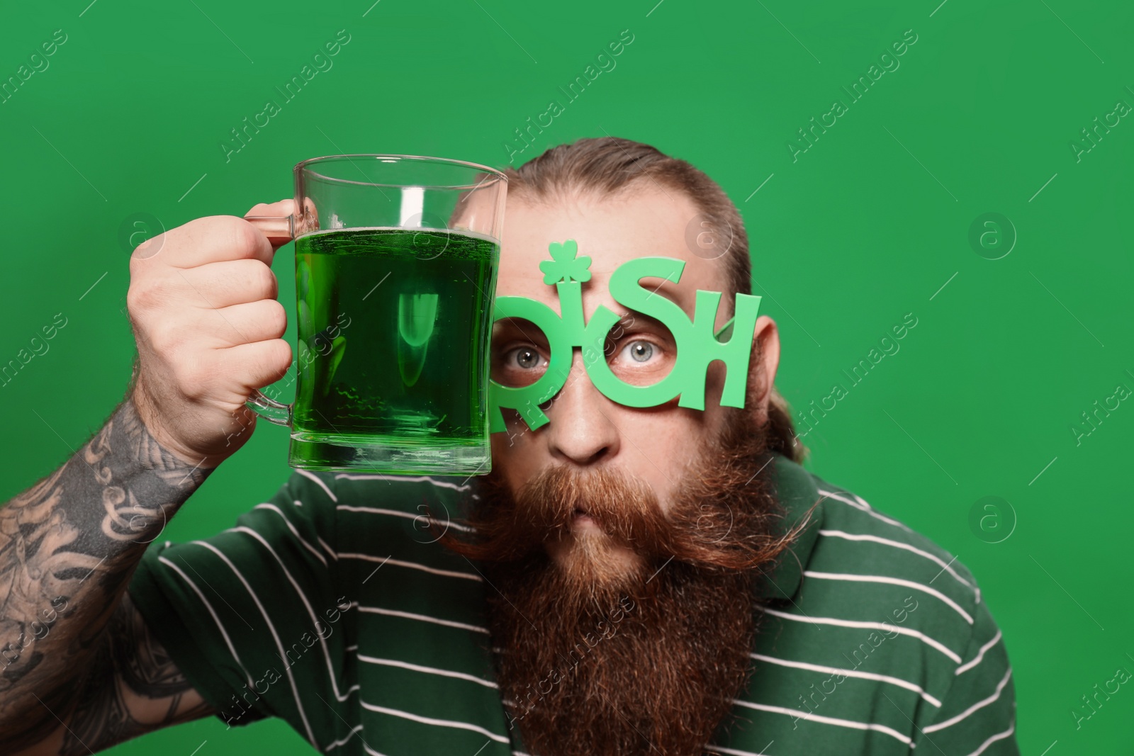 Photo of Bearded man in party glasses with green beer on color background. St. Patrick's Day celebration