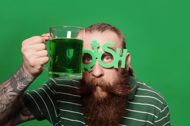 Photo of Bearded man in party glasses with green beer on color background. St. Patrick's Day celebration