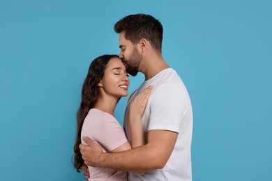 Photo of Man kissing his smiling girlfriend on light blue background