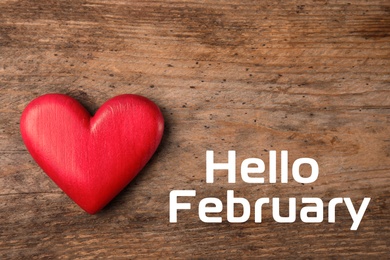 Image of Greeting card with text Hello February. Red decorative heart on wooden background, top view