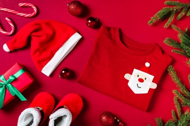 Flat lay composition with cute Christmas baby clothes on red background