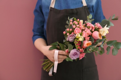 Female florist with beautiful bouquet on color background