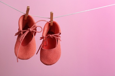 Cute small shoes hanging on washing line against color background, space for text. Baby accessories