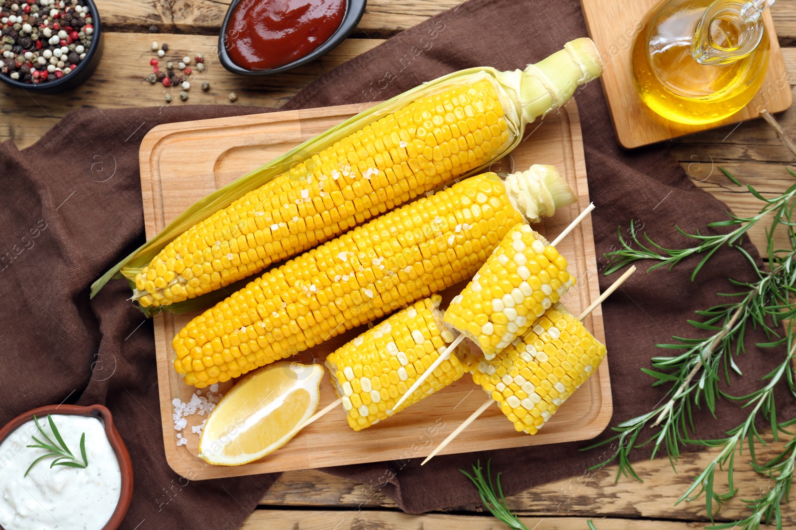 Photo of Tasty cooked corn cobs and products on wooden table, flat lay