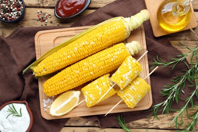 Tasty cooked corn cobs and products on wooden table, flat lay