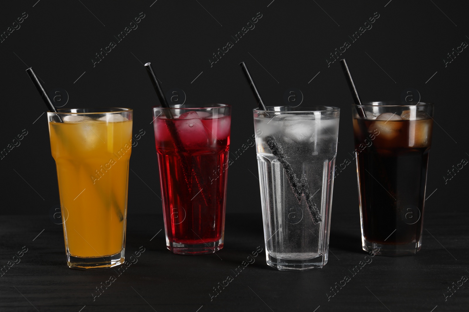 Photo of Glasses of different refreshing soda water with ice cubes and straws on black table