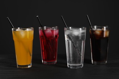 Photo of Glasses of different refreshing soda water with ice cubes and straws on black table