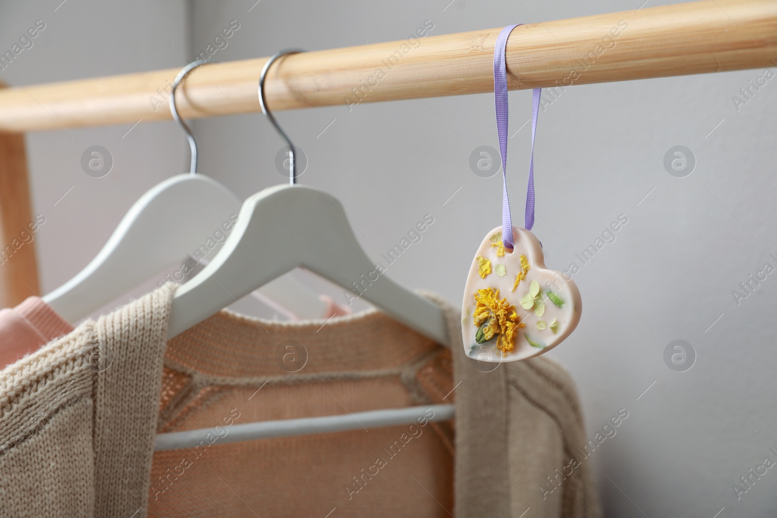 Photo of Beautiful heart shaped scented wax sachet and clothes hanging on wooden rack indoors