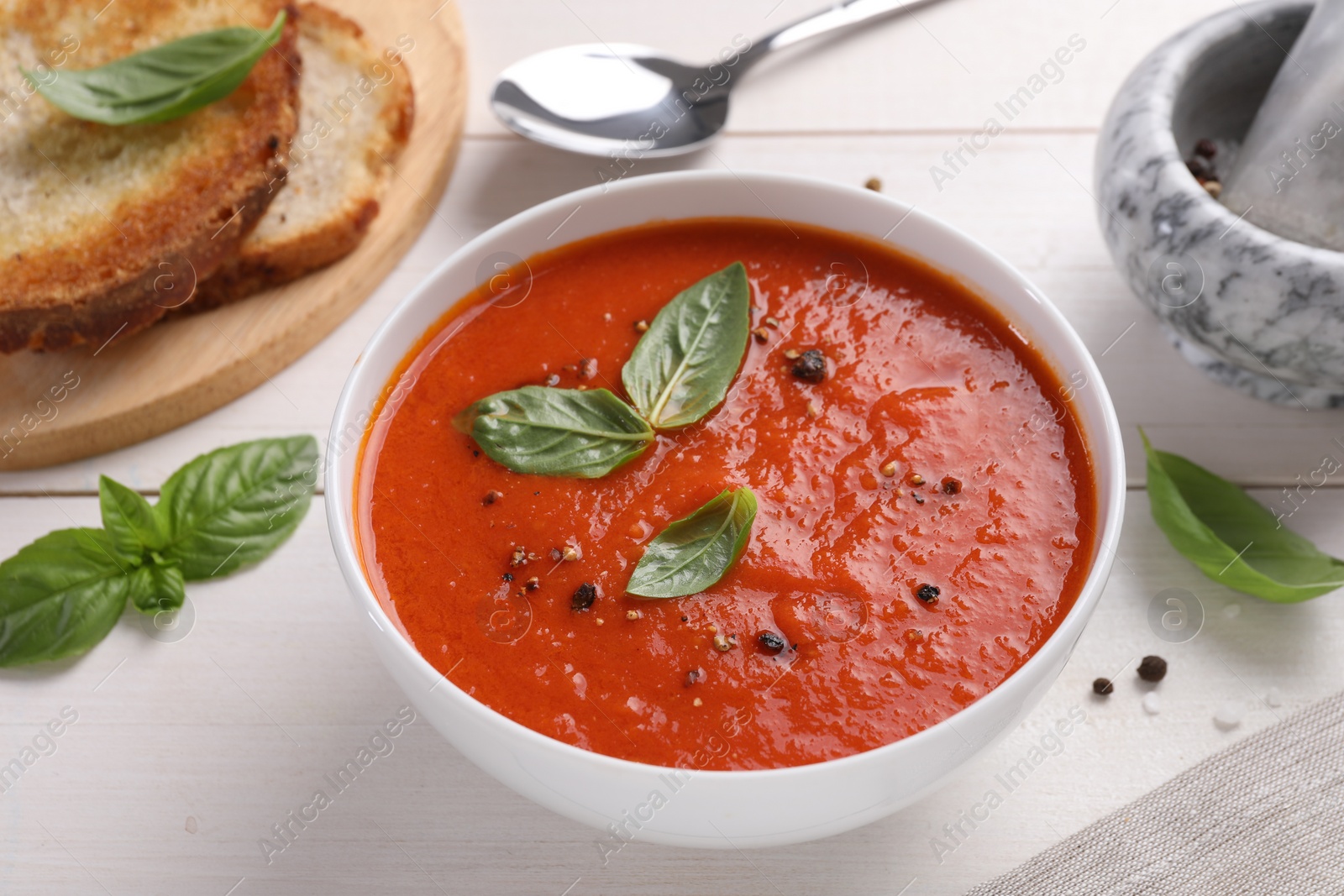 Photo of Delicious tomato cream soup in bowl on white wooden table, closeup