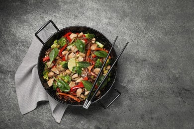 Photo of Stir-fry. Tasty noodles with meat in wok and chopsticks on grey textured table, top view. Space for text