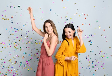 Photo of Happy women and falling confetti on light grey background
