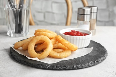 Photo of Slate plate with onion rings and bowl of sauce on table