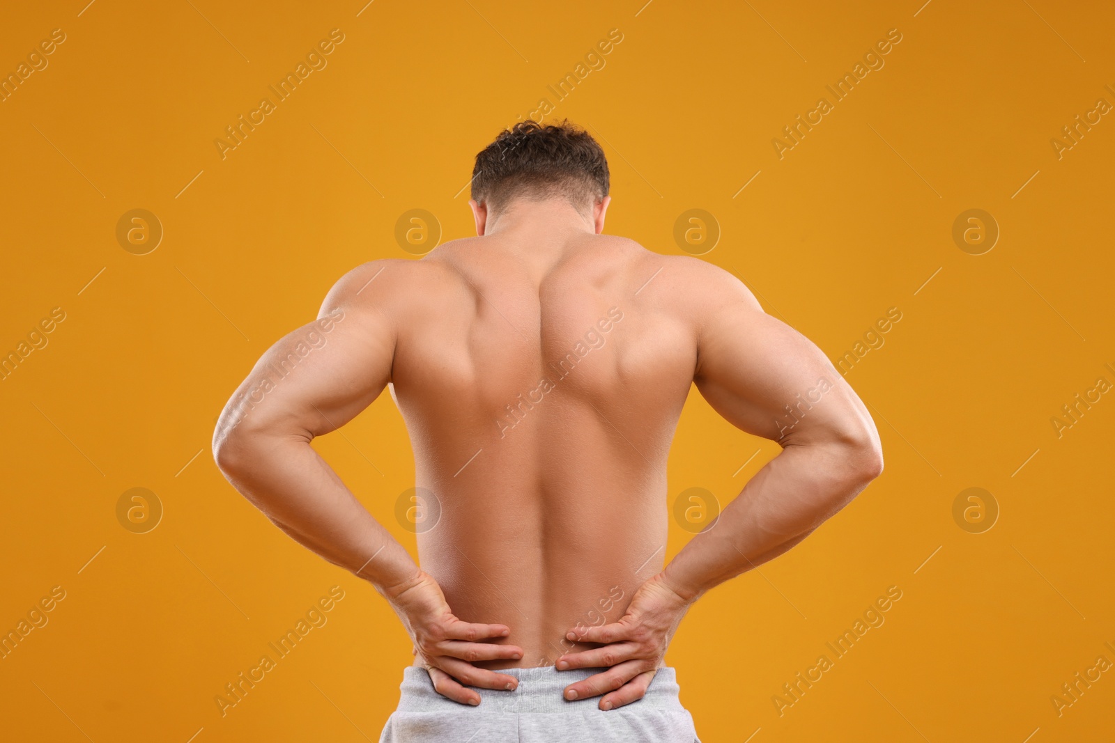 Photo of Man suffering from back pain on orange background, back view