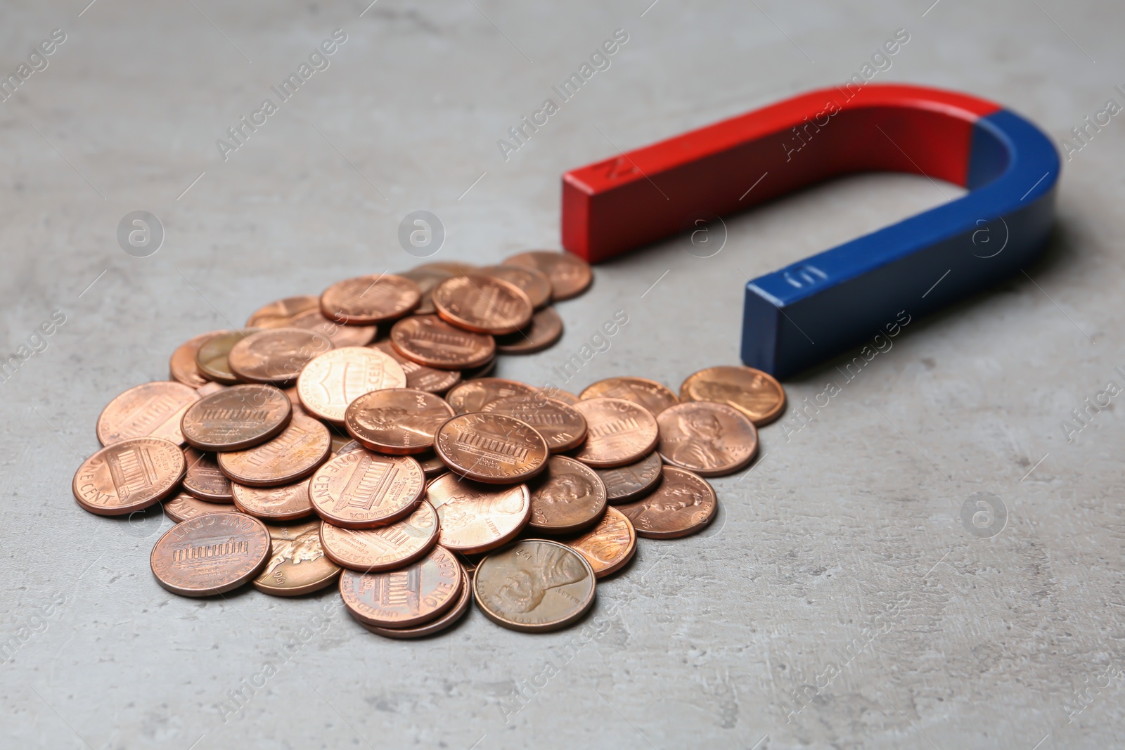 Photo of Magnet attracting coins on grey background, closeup. Business concept