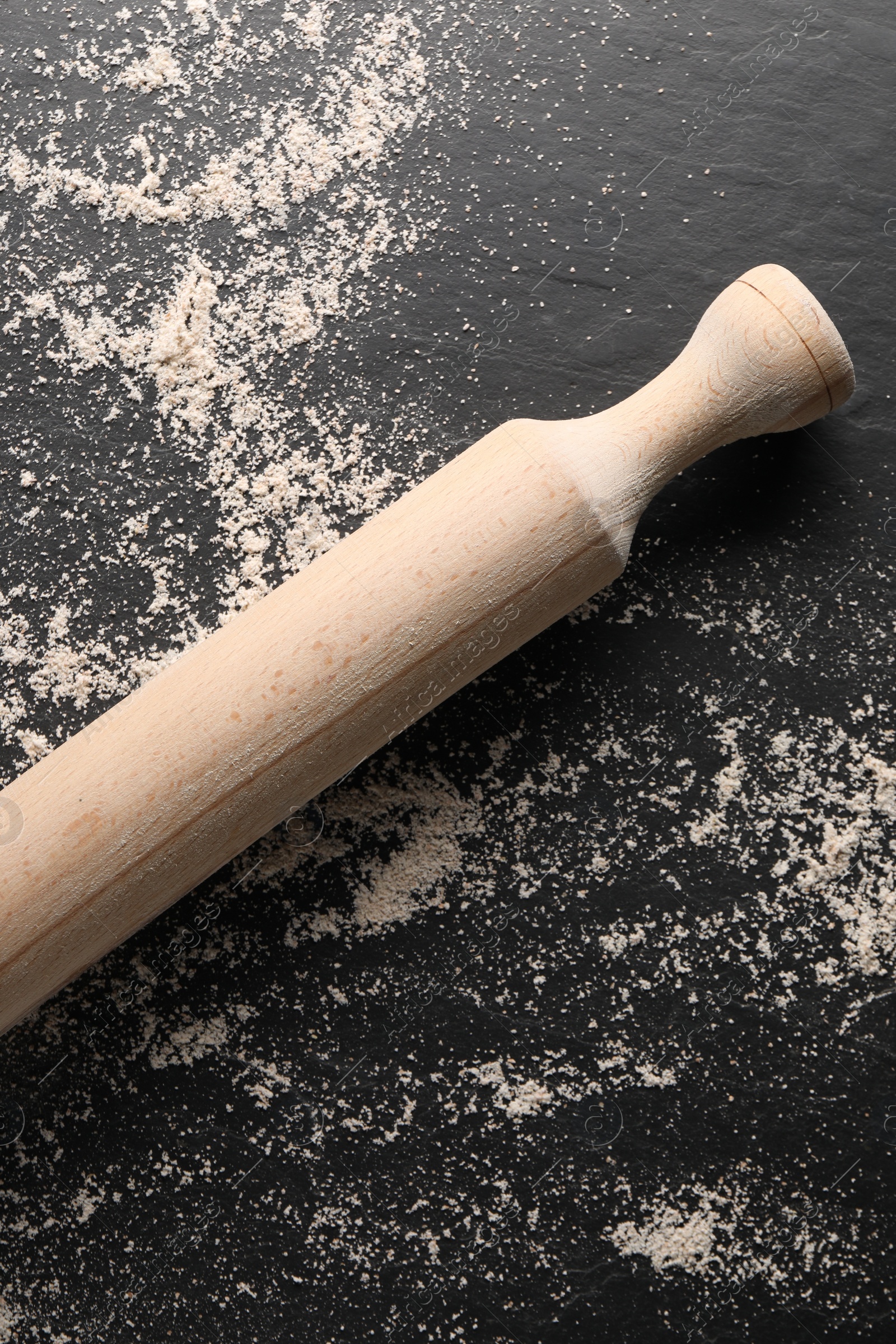 Photo of Scattered flour and rolling pin on black textured table, top view