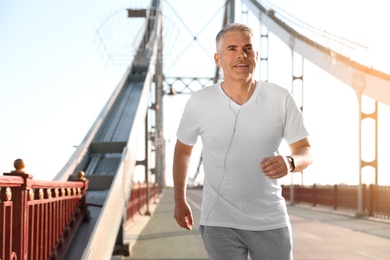 Photo of Handsome mature man running on bridge, space for text. Healthy lifestyle