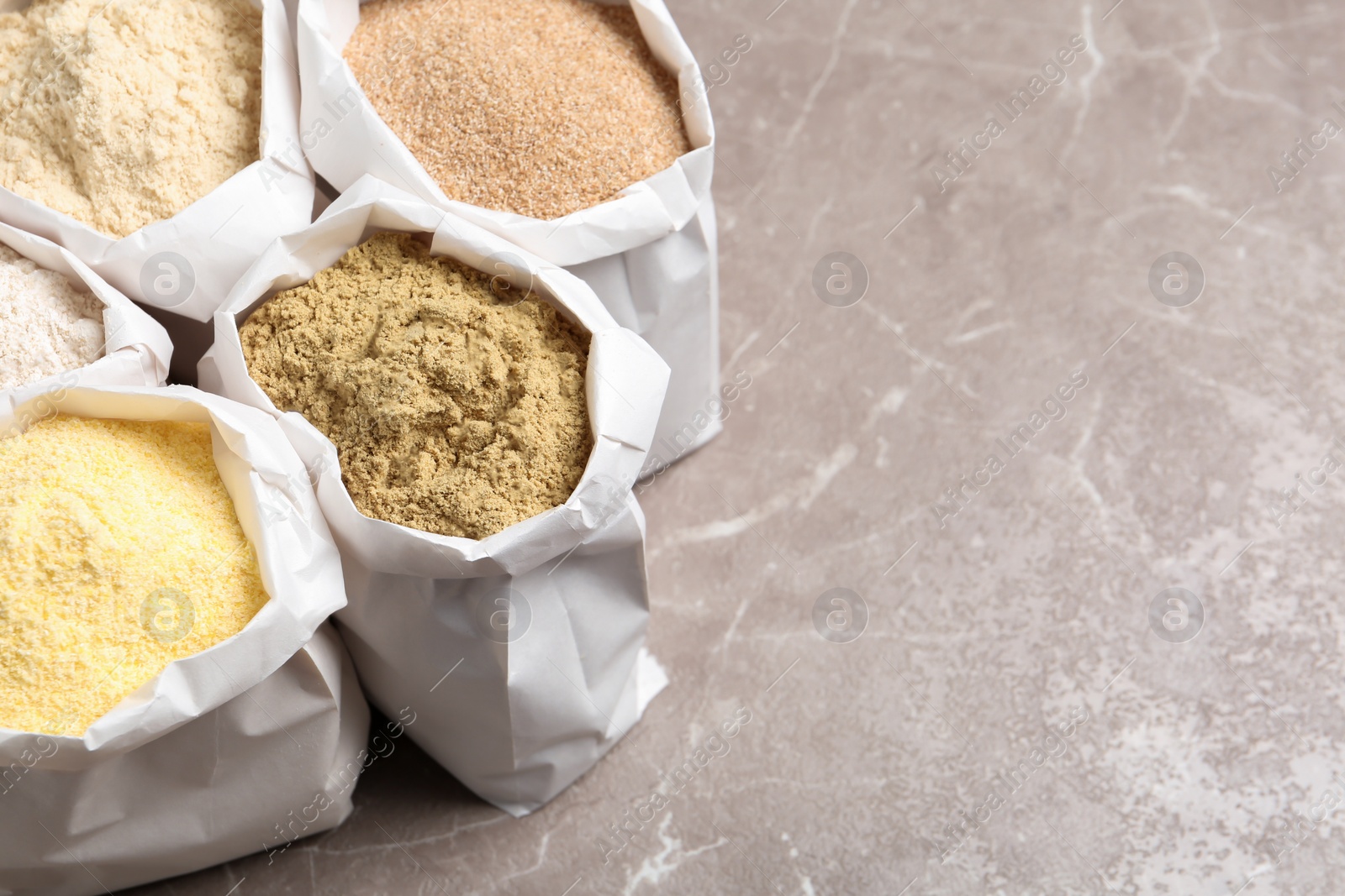 Photo of Bags with different types of flour on grey background. Space for text