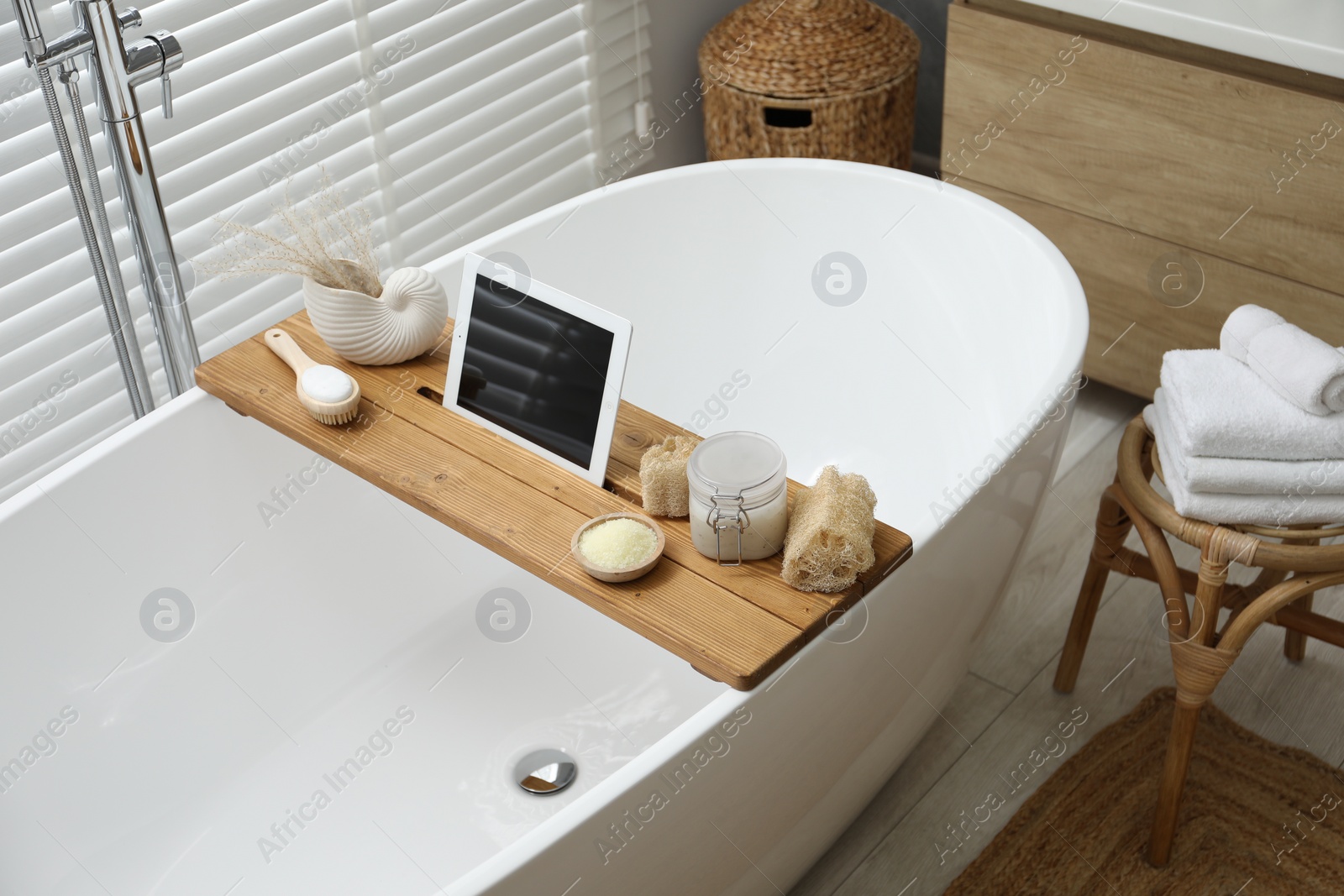 Photo of Wooden tray with tablet and spa products on bath tub in bathroom