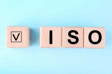 International Organization for Standardization. Wooden cubes with check mark and abbreviation ISO on light blue background, flat lay
