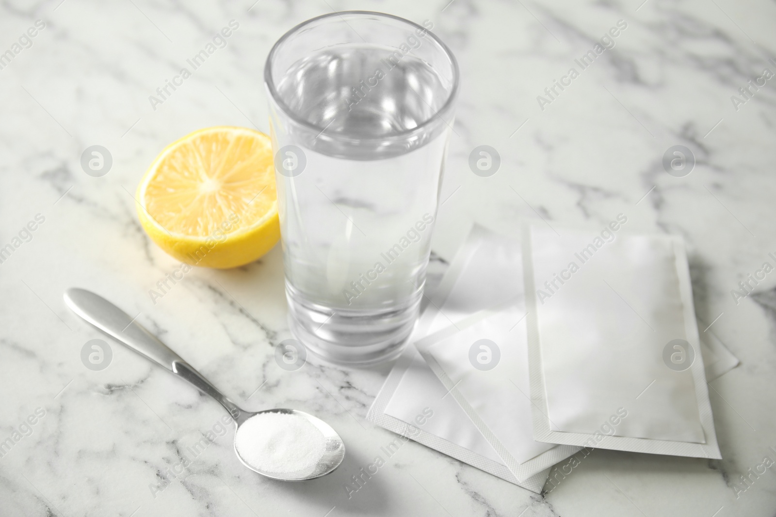 Photo of Medicine sachets, glass of water, spoon and lemon on white table