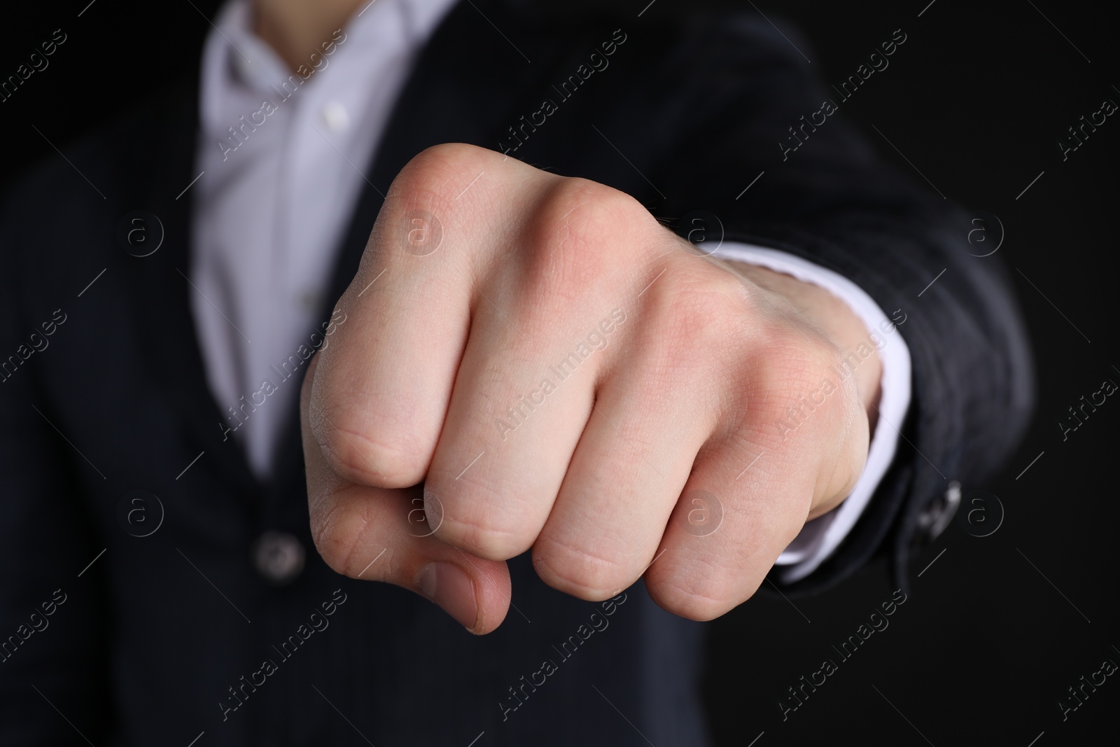 Photo of Businessman showing fist with space for tattoo on black background, closeup