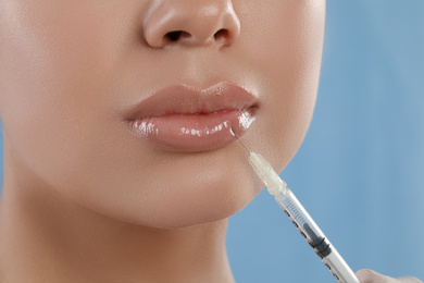 Young woman getting lips injection on light blue background, closeup