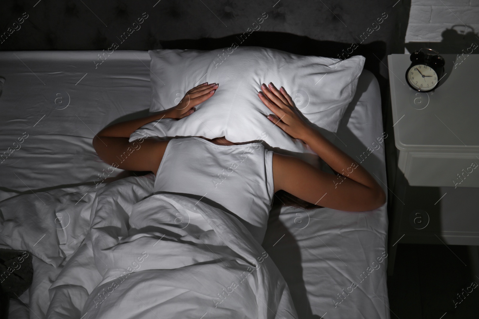 Photo of Young woman covering head with pillow in bed at home. Sleep disorder