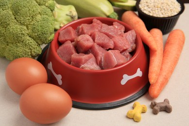 Photo of Raw meat in bowl, products and vitamins for pet on beige background, closeup