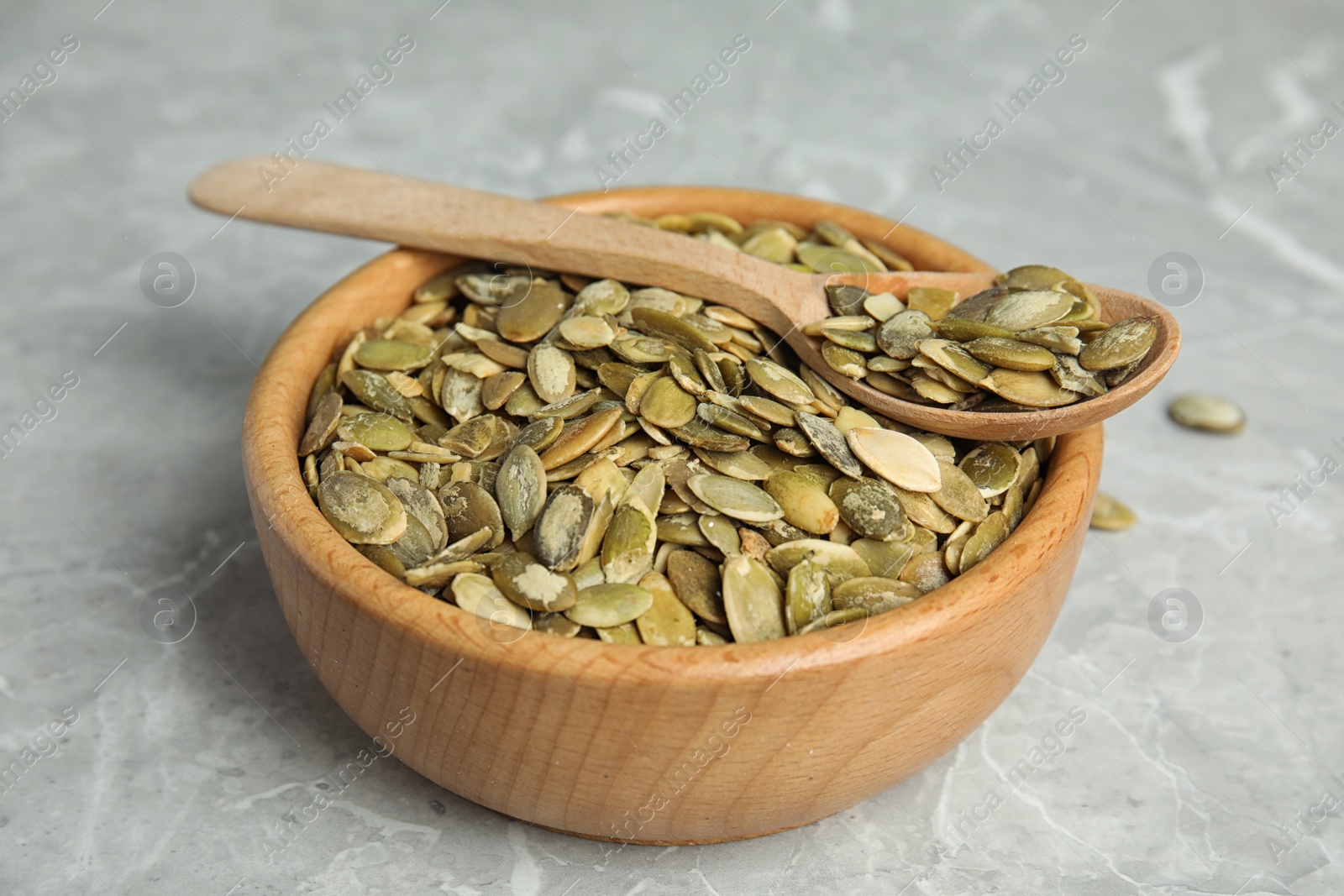 Photo of Bowl and spoon of raw pumpkin seeds on light grey marble table