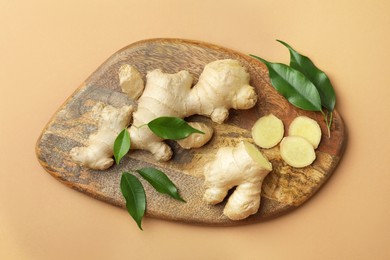 Photo of Fresh ginger with green leaves on light pale brown background, top view