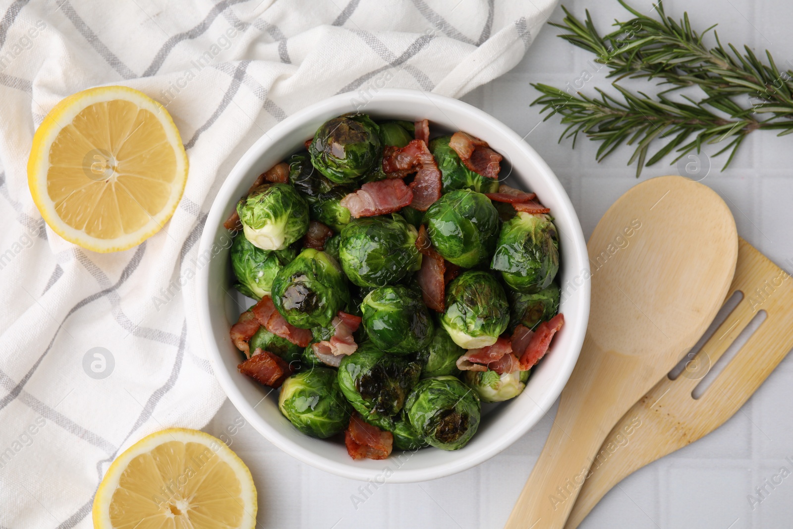 Photo of Delicious roasted Brussels sprouts and bacon served on white tiled table, flat lay
