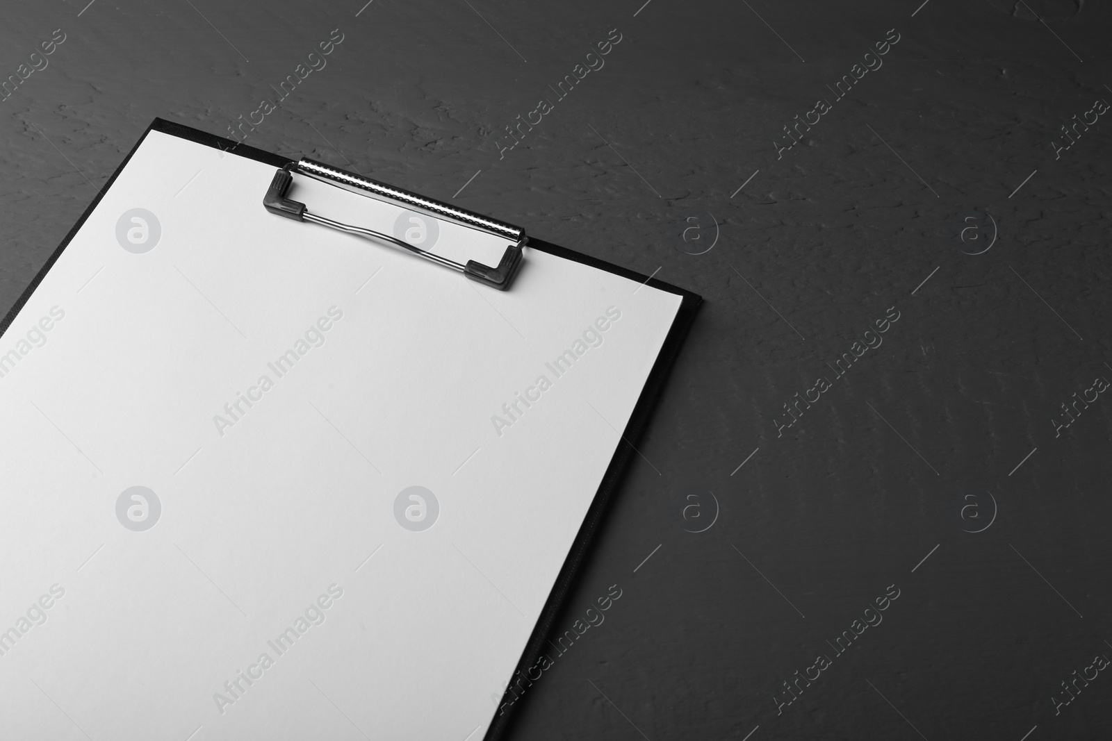 Photo of Clipboard with sheet of paper on black wooden table. Space for text