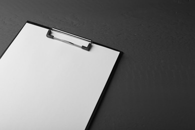 Photo of Clipboard with sheet of paper on black wooden table. Space for text