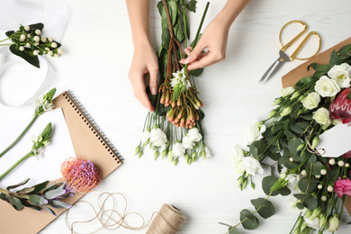 Photo of Florist making beautiful bouquet at white wooden table, top view