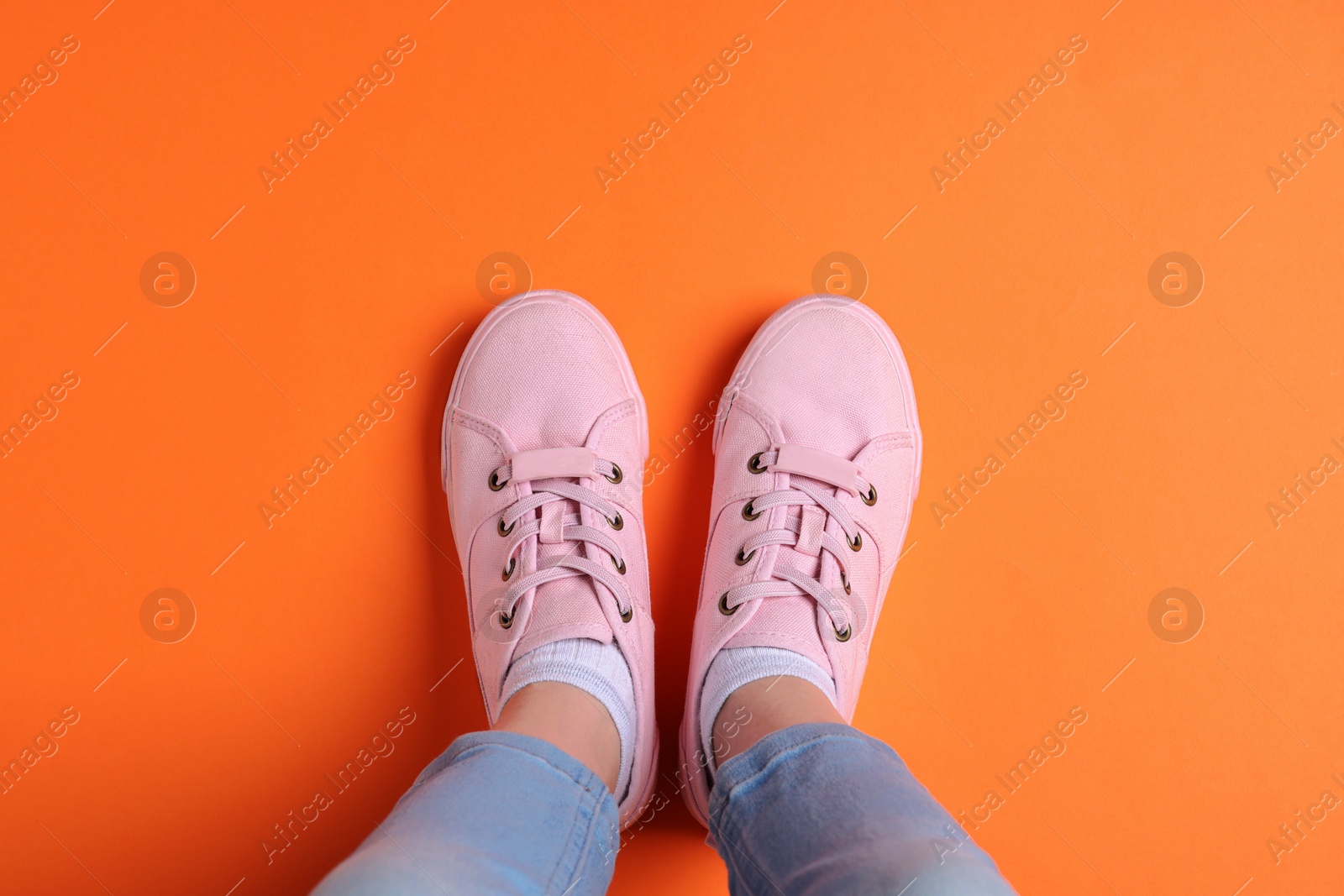 Photo of Woman in stylish sneakers standing on orange background, top view