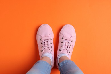 Photo of Woman in stylish sneakers standing on orange background, top view