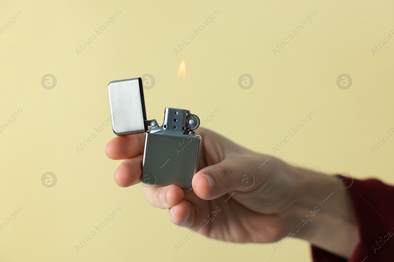 Photo of Man holding lighter with burning flame against beige background, closeup