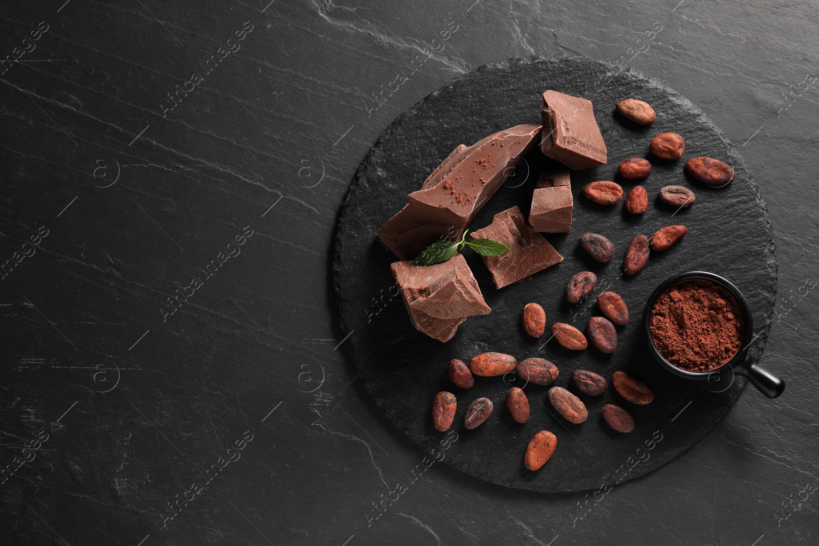 Photo of Pieces of tasty milk chocolate, cocoa beans, powder and mint on grey textured table, top view. Space for text