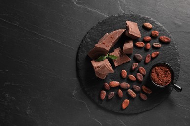 Photo of Pieces of tasty milk chocolate, cocoa beans, powder and mint on grey textured table, top view. Space for text