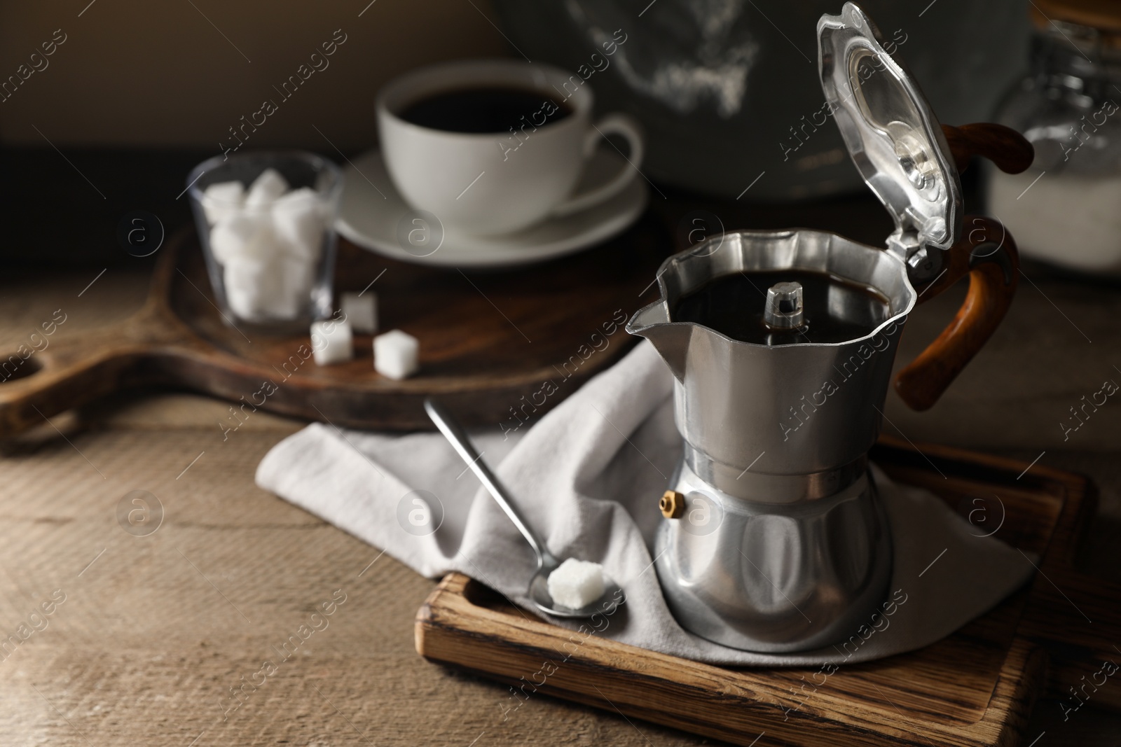 Photo of Brewed coffee in moka pot and sugar cube on wooden table, space for text